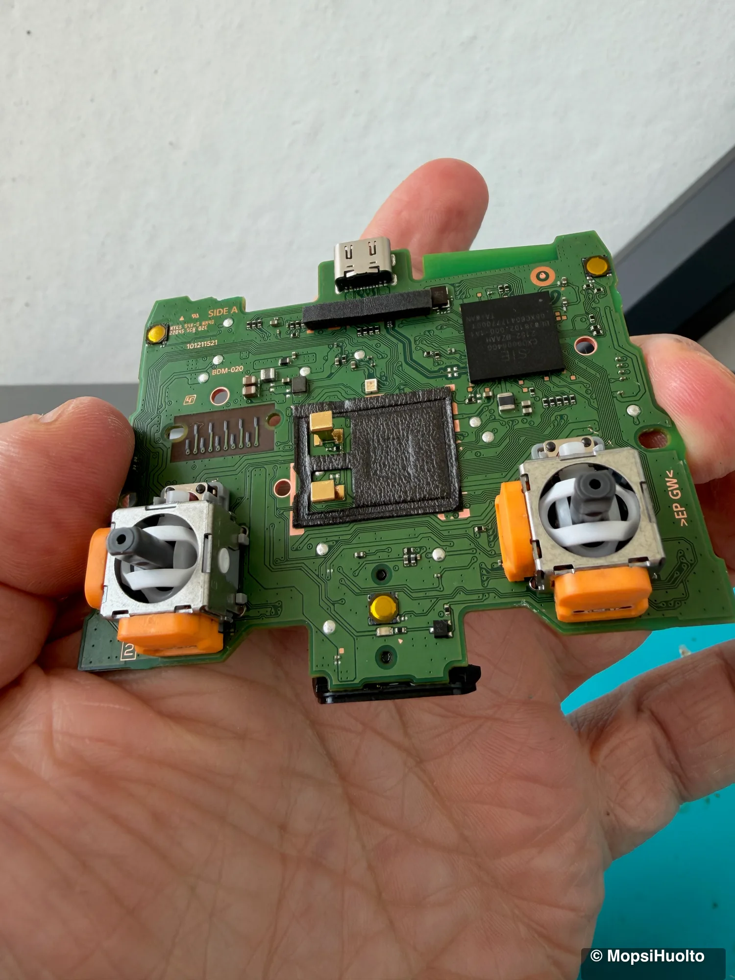 DualSense main board held in a hand, both analog stick modules with their orange side housings in view.